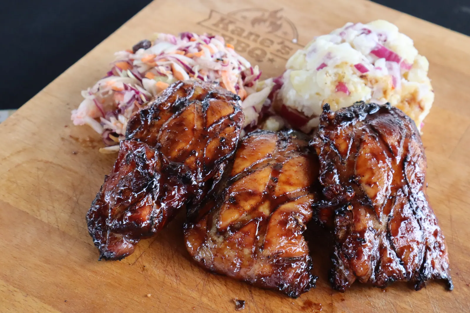 Kippendijen met coleslaw en aardappelsalade op een plank